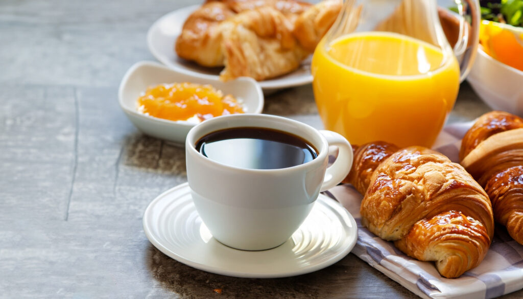 mesa de café da manhã composto por uma xícara de café, geleia, croissants e suco de laranja