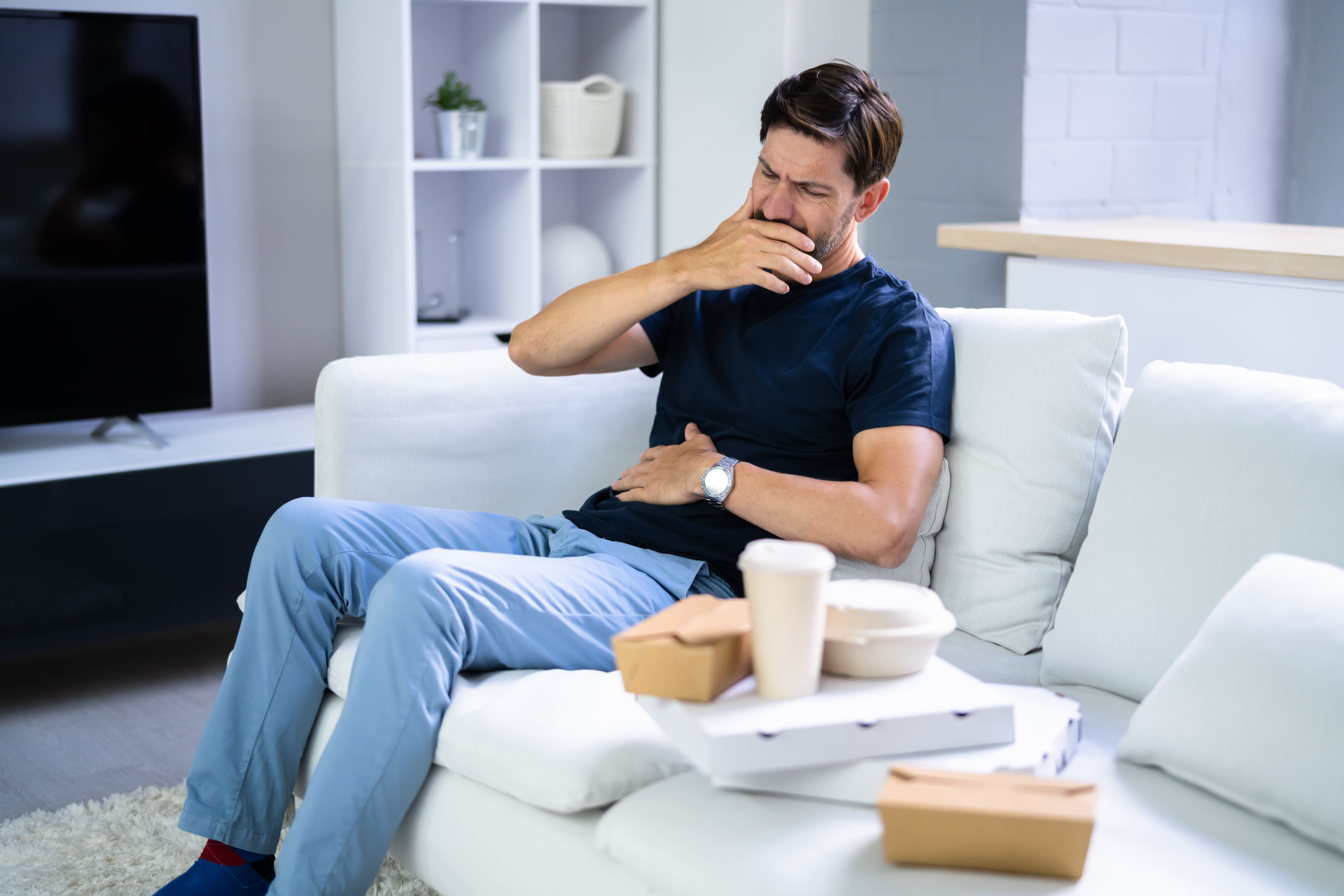 homem sentado no sofá sofrendo de desconforto gástrico azia