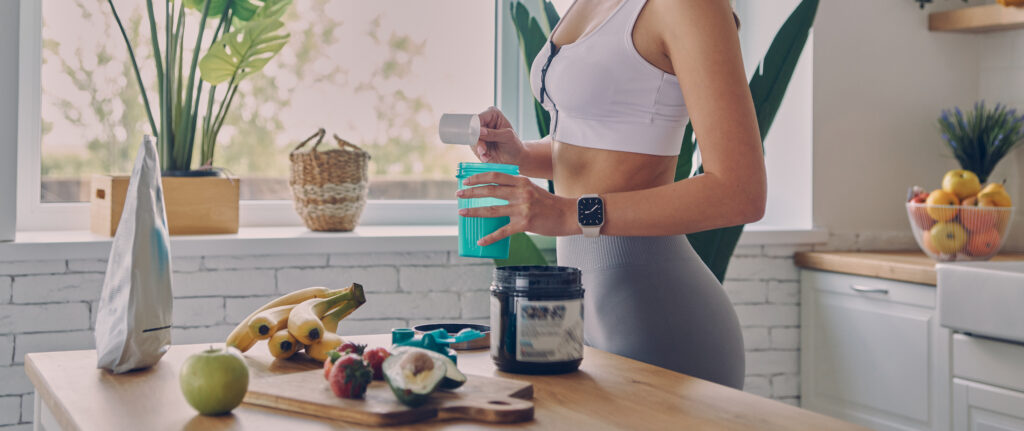 mulher em roupas esportivas preparando whey na cozinha