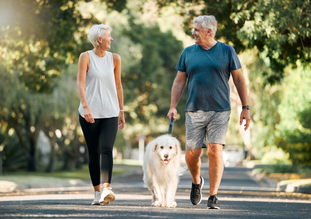 casal de homem e mulher idosos fazendo caminhada ao ar livre com cachorro golden