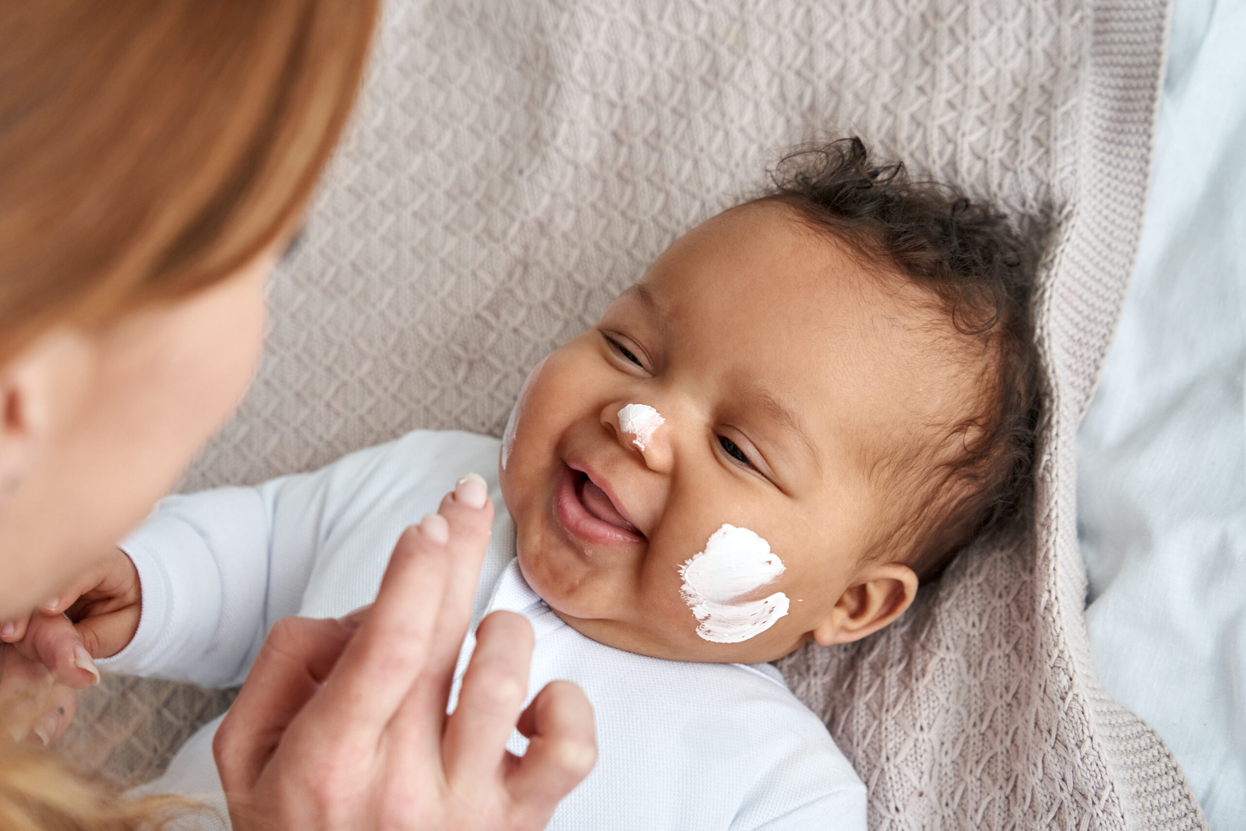 Mãe aplicando Babycreme Weleda com calêndula na pele do bebê durante troca de fraldas